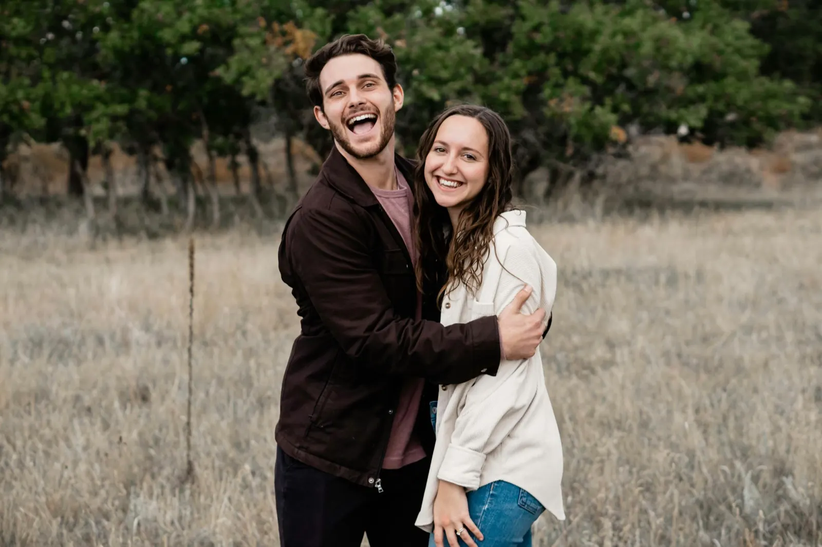 Un couple souriant s’enlace dans un champ d’herbes hautes