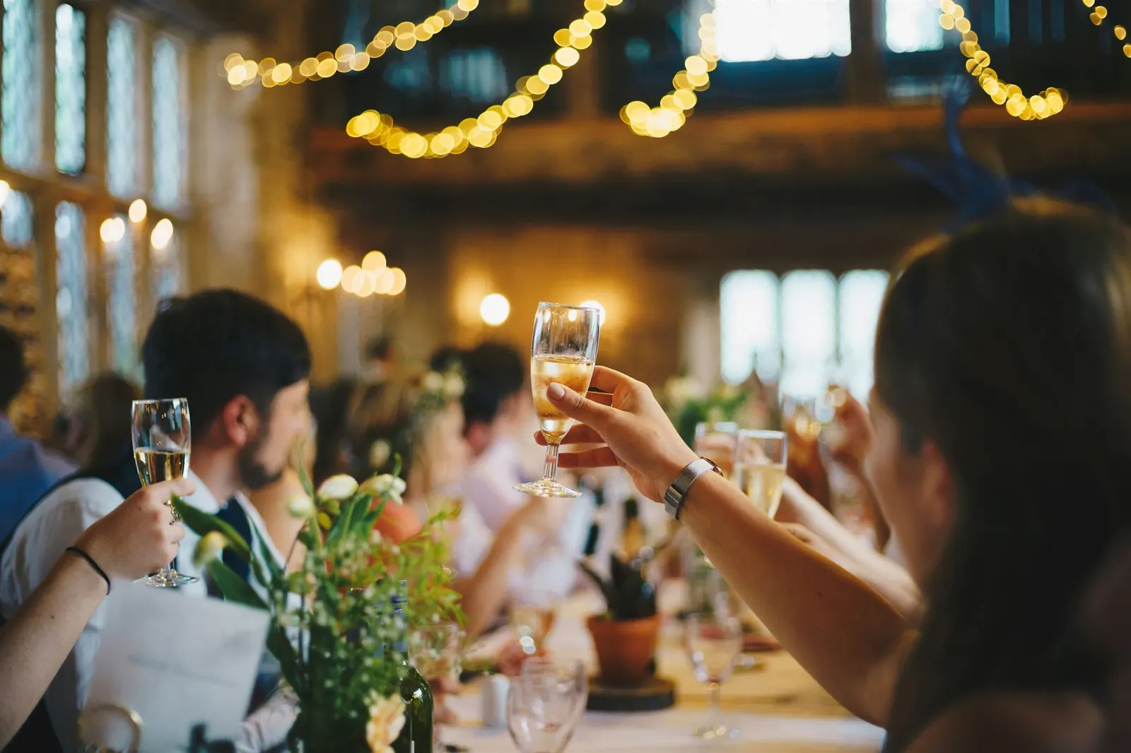 Des invités trinquent au champagne lors d’un repas de mariage, sous des guirlandes lumineuses