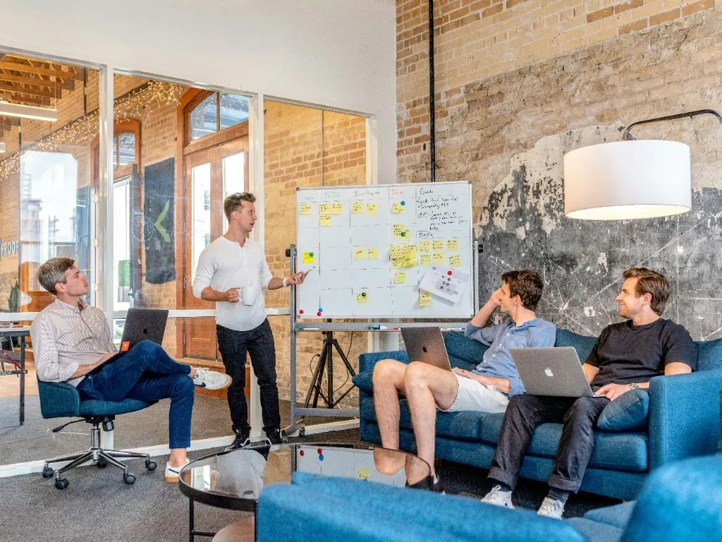 Atelier d’équipe : un animateur devant un tableau couvert de post-it, collègues assis sur des canapés