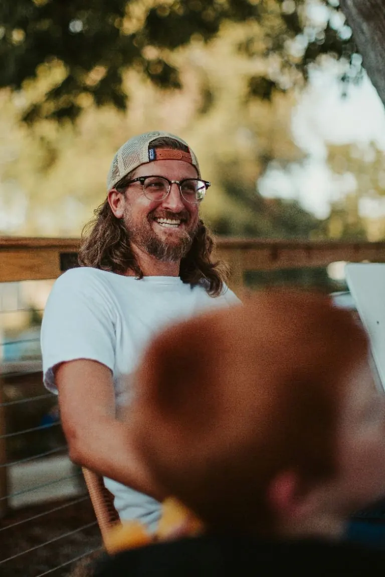 Un homme souriant en casquette et lunettes lors d’une fête d’été en fin de journée