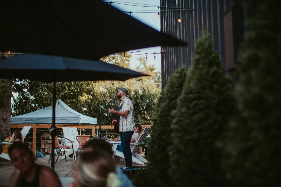 Un musicien joue sur une terrasse en plein air, entre parasols et arbres
